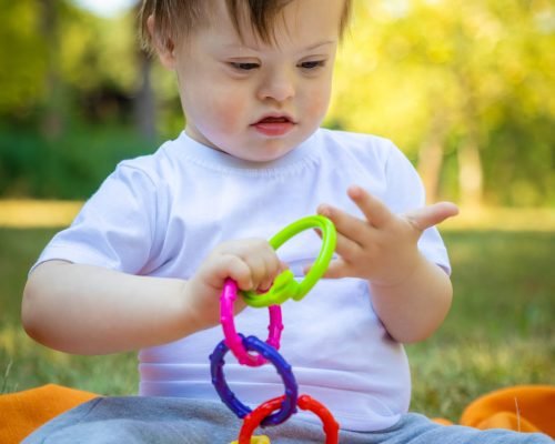Portrait of Cute small boy with Down syndrome playing on blanket in summer day on nature with toys