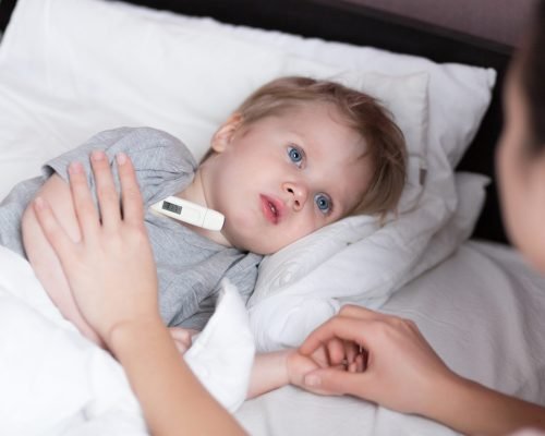 Sick child boy laying in bed and mom hand taking temperature. Mother checking temperature of her sick son. Sick child with fever and illness in bed at home.